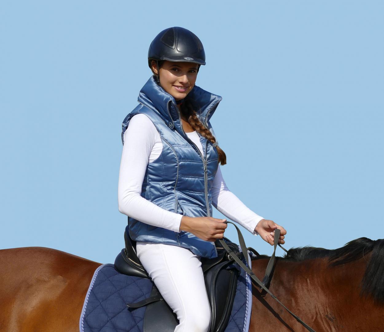 Frau sitzt mit stylischer blauer Weste auf einem Pferd