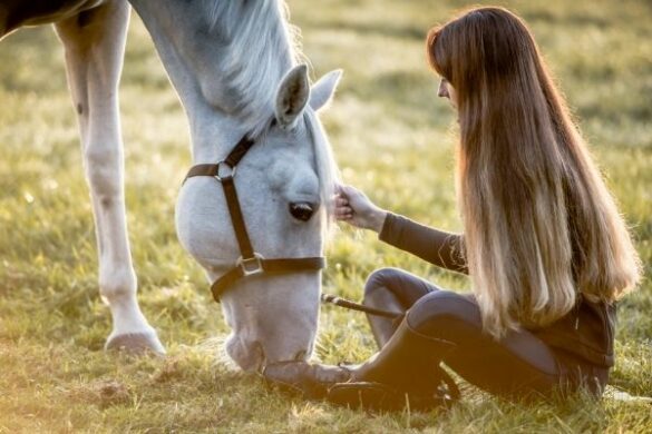 Fotoshooting Pferd Ideen: Frau sitzt auf einer Wiese und ihr Pferd grast neben ihr.