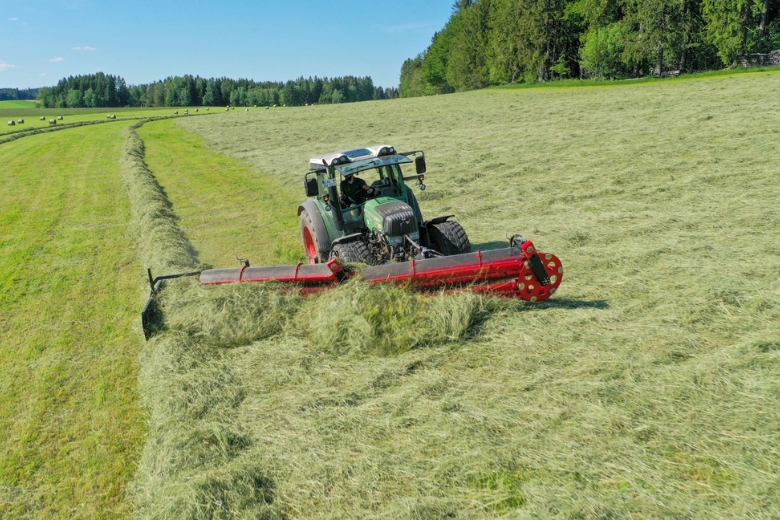 Heu trocknen: Traktor fährt über Wiese und wendet Heu