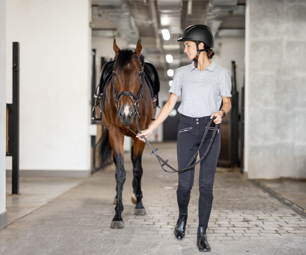Eine Frau führt ein Pferd über eine Stallgasse
