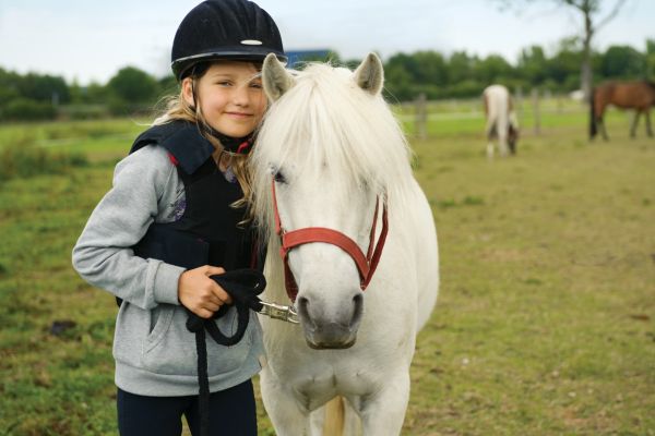 Unterschied Pony Pferd: Kind und Pony stehen auf Feld.