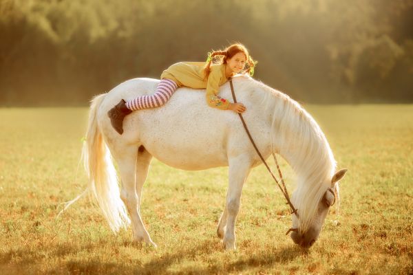 Berühmte Pferdenamen: Mädchen mir roten Haaren liegt auf weißem Pferd