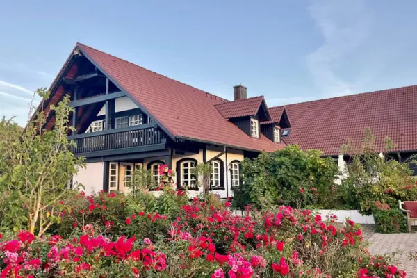Reitanlagen-Gebäude im Fachwerkstil hinter einem üppig blühenden Beet mit kräftig pinken Rosen.
