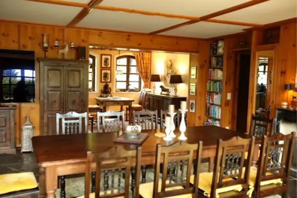 Rustikaler Aufenthaltsraum mit einem langen Holztisch, Stühlen mit gelben Kissen und warmen Holzverkleidungen an Wänden und Decke.