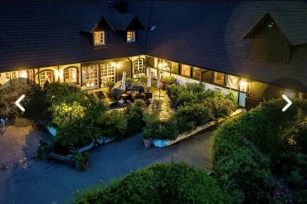 Abendliche Luftaufnahme eines beleuchteten Innenhofs einer exklusiven Reitanlage mit Bepflanzung und Terrasse.