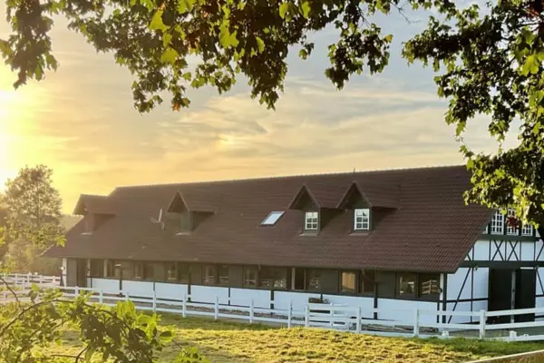 Ein langgestrecktes Stallgebäude einer Reitanlage im Fachwerkstil bei warmem Sonnenuntergangslicht.