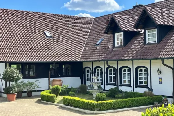 Gepflegter Innenhof einer Reitanlage im Fachwerkstil mit einem mehrstufigen Zierbrunnen und niedrigen Hecken.