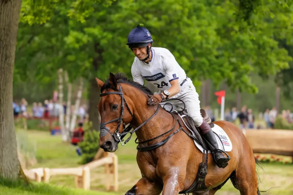 Vielseitigkeitsreiter Harry Meade lobt lächelnd sein schweißglänzendes braunes Pferd während eines Geländeritts auf einem grünen Turnierkurs. Foto: Archiv sportfotos-lafrentz.de