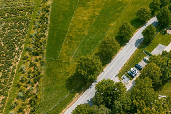 Luftaufnahme von weitläufigen, eingezäunten Pferdewiesen an einer Landstraße mit Parkplatz.