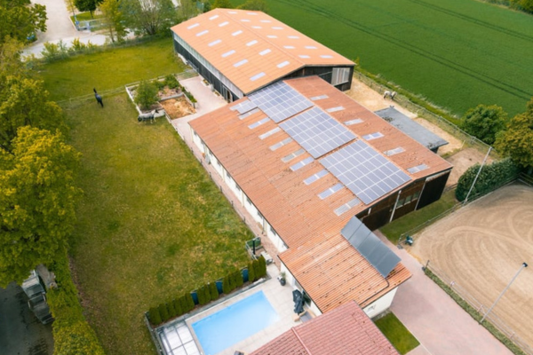 Draufsicht auf das Reitgut mit Hallendächern, Solaranlage, privatem Poolbereich und Wiesen.