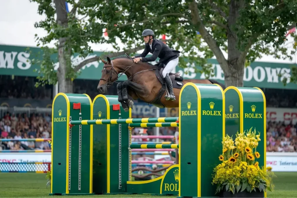 Springreiter Richard Vogel auf dem braunen Hengst United Touch S im Flug über ein grünes Rolex-Hindernis beim Reitturnier in Spruce Meadows.